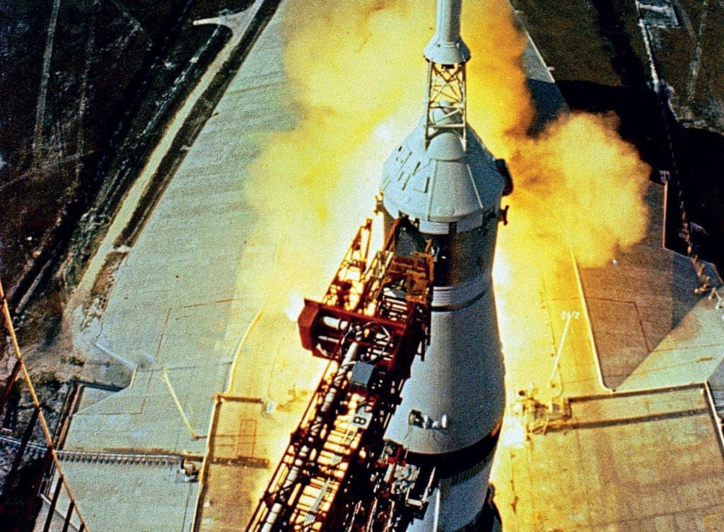 Seconds before lift-off, a fish-eye lens camera high up on the Launch Umbilical Tower casts a dramatic view of the five F-1 engines running up to full thrust before release. Note the white boost protective cover (BPC) supporting the launch escape system (LES) encapsulating the Command Module. (NASA)